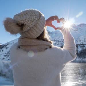 Frau am winterlichen See herzt Sonne mit den Händen
