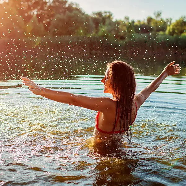 Eine junge Frau im Bikini spielt im Wasser und spritzt dabei Wasser um sich herum.